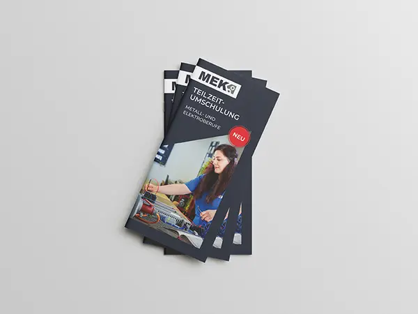 Stapel von drei gefächerten DIN Lang Flyern zur Teilzeitumschulung auf grauem Hintergrund.