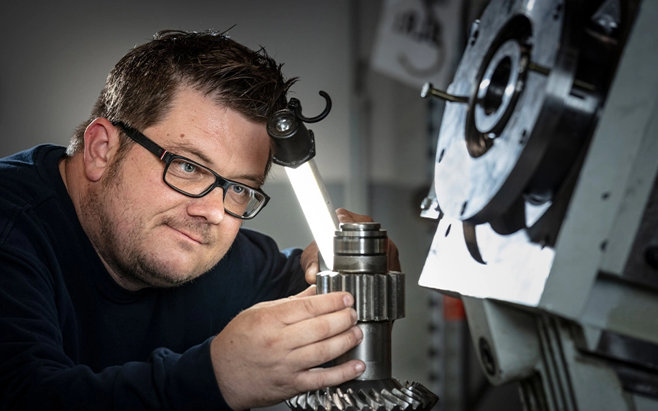 Mitarbeiter im Maschinenbau in Arbeitskleidung überprüft ein Getriebe im Rahmen der Instandhaltung, um die ordnungsgemäße Funktion der Maschine sicherzustellen.