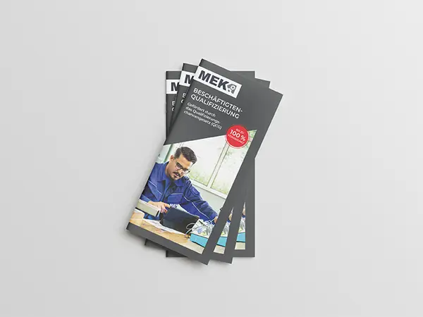 Stapel von drei gefächerten DIN Lang Flyern zur Beschäftigtenqualifizierung auf grauem Hintergrund.