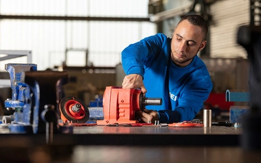 Teilnehmer in MEK-Arbeitskleidung arbeitet an einem Getriebe im Rahmen der Umschulung zum Industriemechaniker.