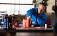 Teilnehmer in MEK-Arbeitskleidung arbeitet an einem Getriebe im Rahmen der Umschulung zum Industriemechaniker.