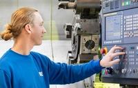 Teilnehmer einer Umschulung zum Zerspanungsmechaniker bedient das Bedienpanel einer CNC-Drehmaschine in der MEK-Werkstatt.