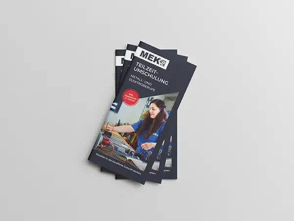 Stapel von drei gefächerten DIN Lang Flyern zur Teilzeitumschulung auf grauem Hintergrund.