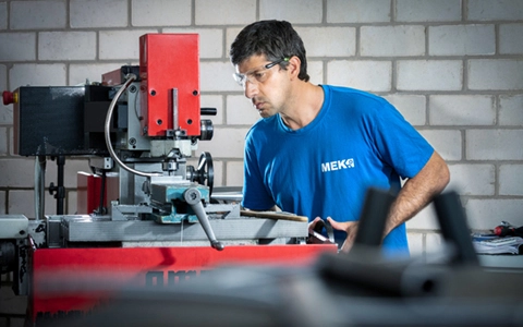 Teilnehmer der Umschulung zur Fachkraft für Metalltechnik – Zerspanungstechnik arbeitet an einer konventionellen Fräsmaschine in MEK-Arbeitskleidung.