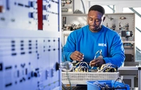 Teilnehmer in der Umschulung zum Mechatroniker arbeitet in der Elektro-Ausbildungswerkstatt an einem technischen Gerät und wendet seine Fachkenntnisse an.