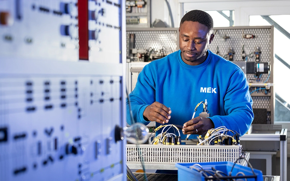 Teilnehmer in der Umschulung zum Mechatroniker arbeitet in der Elektro-Ausbildungswerkstatt an einem technischen Gerät und wendet seine Fachkenntnisse an.